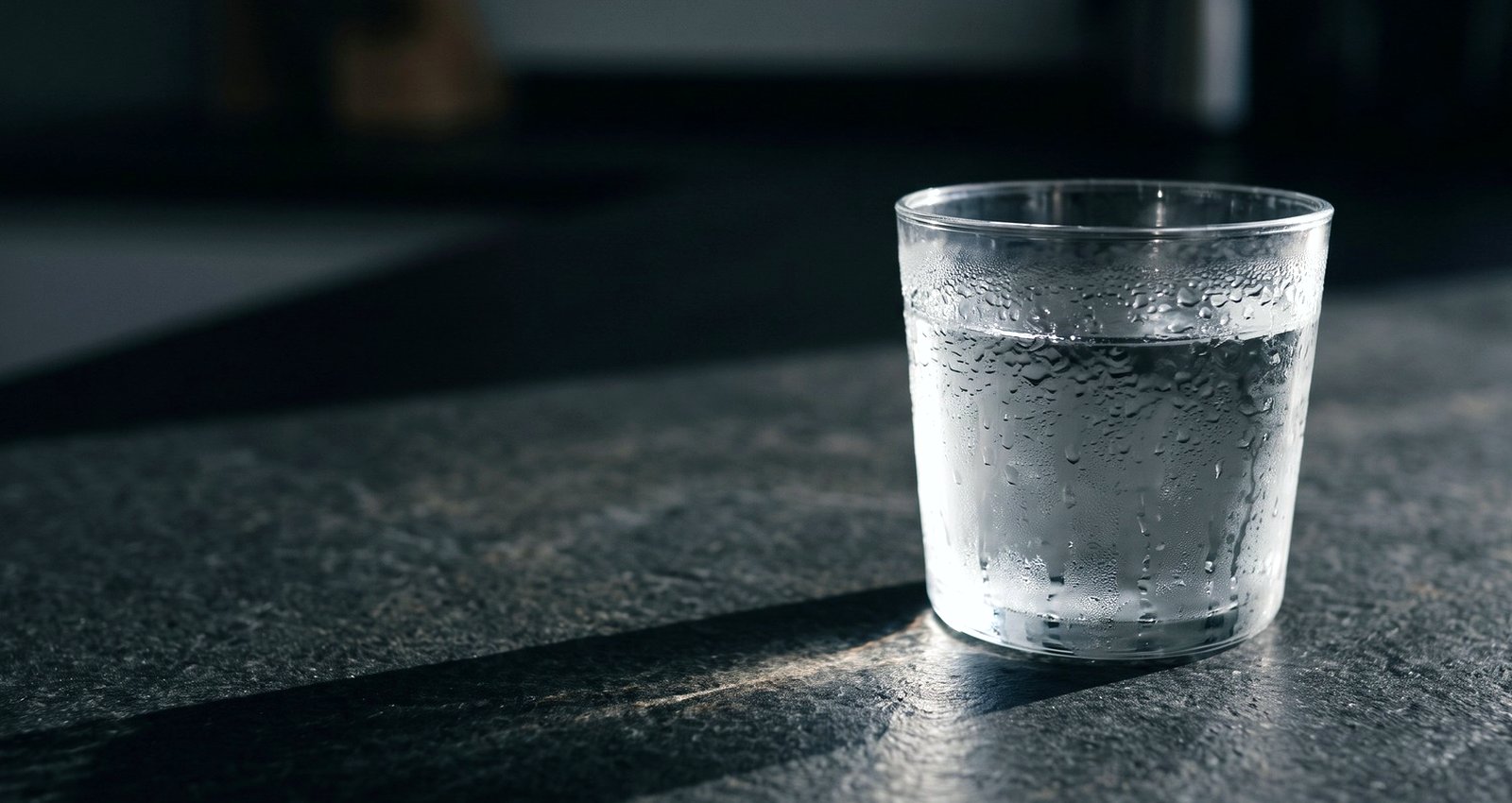 A glass of water on a stone counter in hard morning light